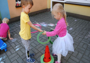 na tarasie chłopiec i dziewczynka wkładają zielone obręcze na czerwony pachołek
